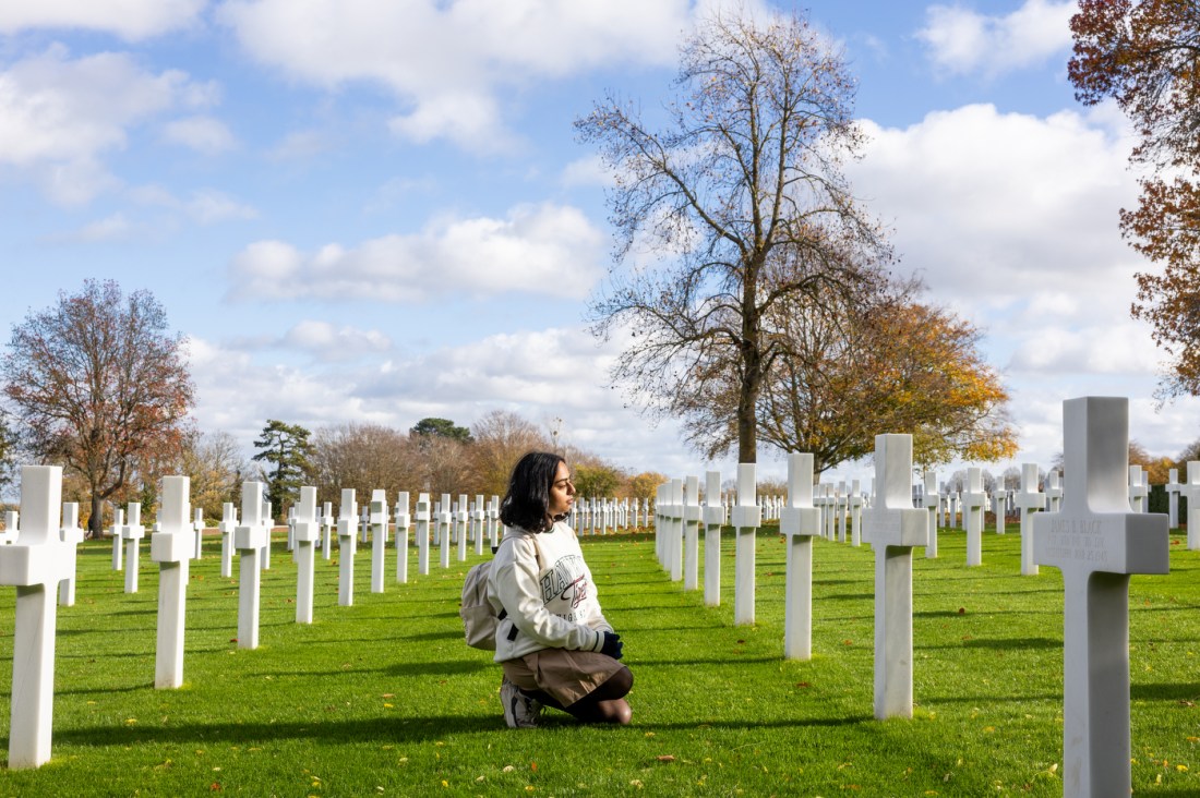 A student looks at rows of white cross markers at the Cambridge American Cemetary.