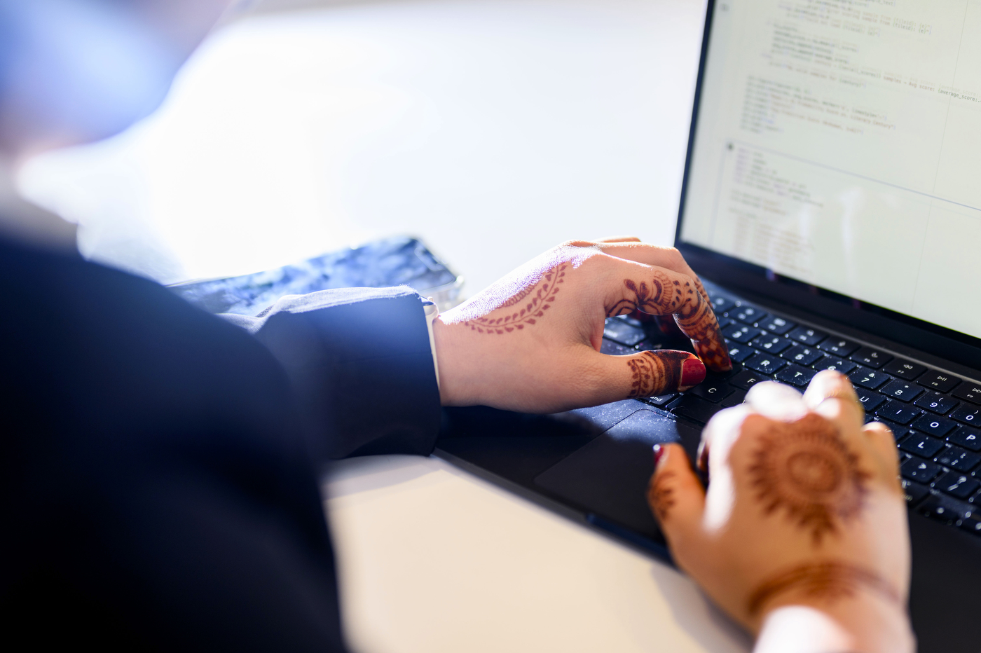 Sohni Rais typing on a laptop. Her hands are poised over the keyboard and have henna tattoos on them. 