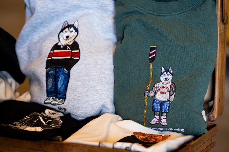 Two folded sweaters, one grey and one green, with embroidered huskies on them folded and laid next to each other. 