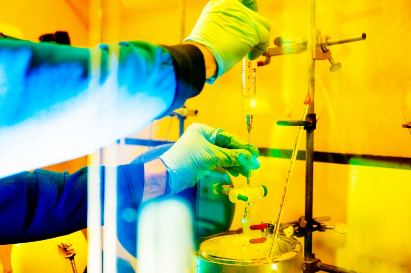 A researcher's hands wearing blue gloves adjusting lab equipment in a lab bathed in yellow lighting. Just their arms and hands are in frame. 