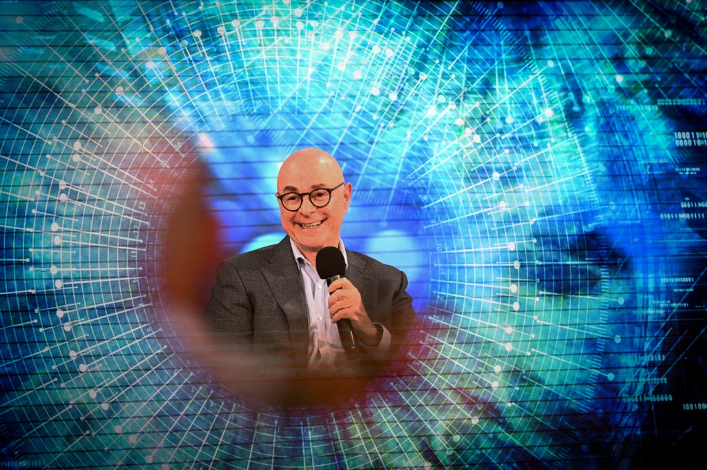 President Joseph E. Aoun holds a microphone and smiles in a blue portrait.