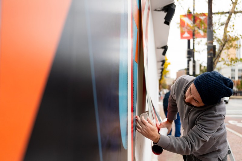 An artist installs a vinyl art print on a wall on the Boston campus.