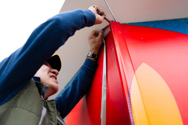 An artist installs a vinyl art print on a wall on the Boston campus.