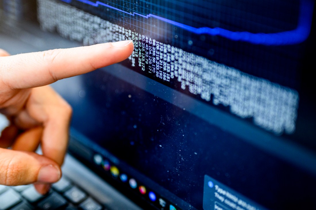 A finger pointing at a blue-lit computer screen displaying lines of code.