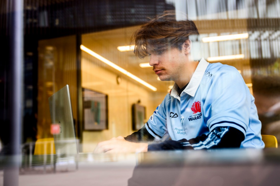 Daniel Sheehan sitting while at work on a laptop, with a brightly lit room in the background.