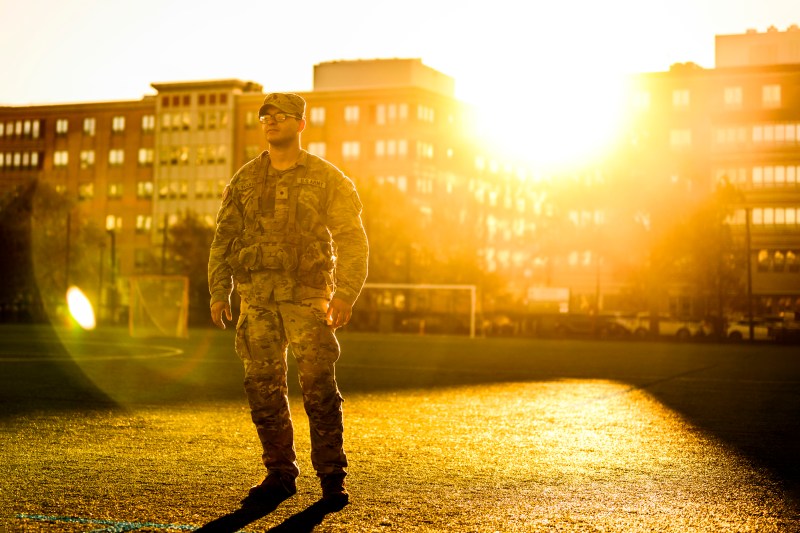 Christian Figueroa posing in his ROTC gear on a turf field with the sunrise behind him. 