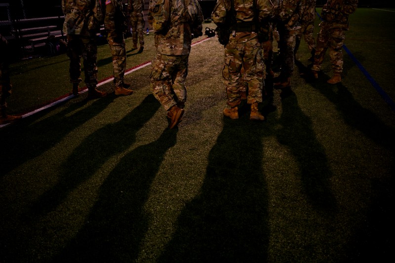 A group of ROTC members in camouflage gearstanding on a dimly lit turf field. 