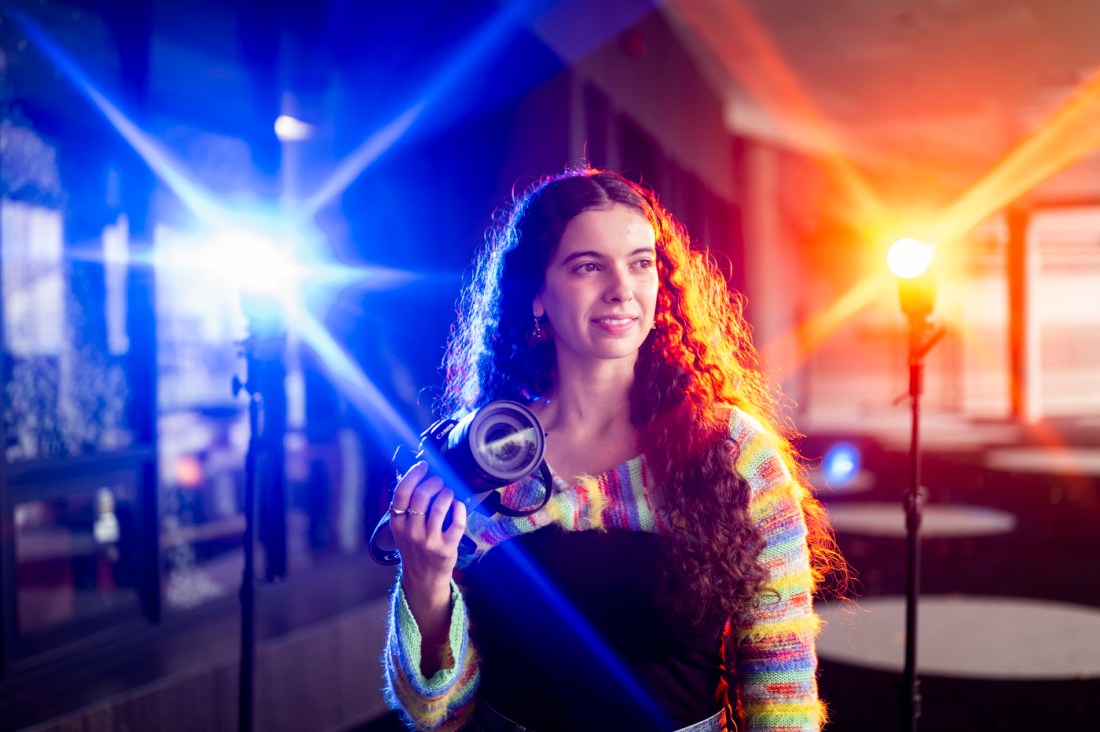 Northeastern alum Samantha Davidson holding her camera as blue and red lights flash on either side of her.
