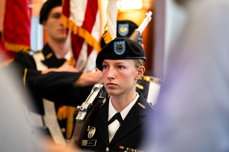 A student in military dress uniform and beret stands attention during a Veterans Day ceremony.