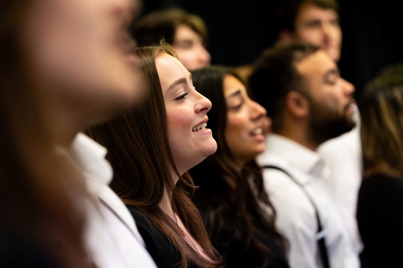 A group of people all singing together, wearing white and black. 