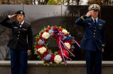 Two students, both of whom are dressed in their military uniforms, salute next to a wreath in front of the Veterans Memorial on Northeastern&#039;s Boston campus.