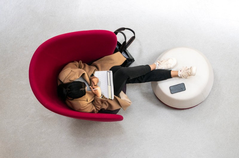 A member of the Northeastern community sits on an armchair with their feet up on a stool in ISEC.