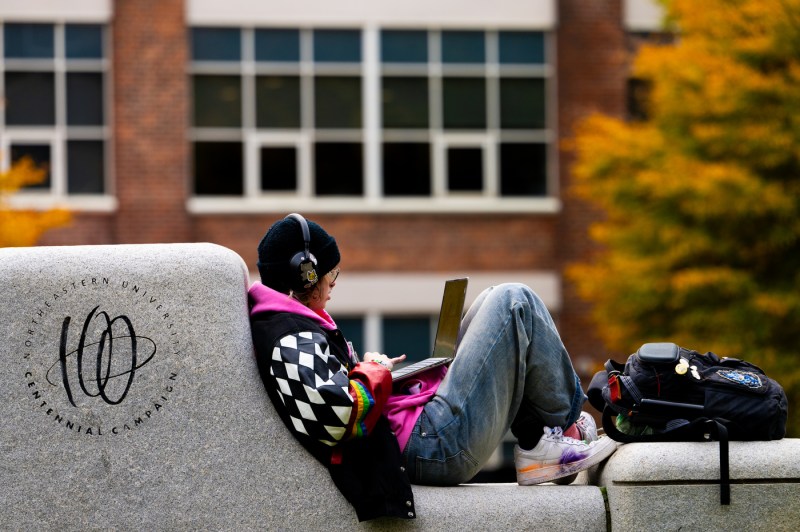 A student sits on a stone wall on the Boston campus.