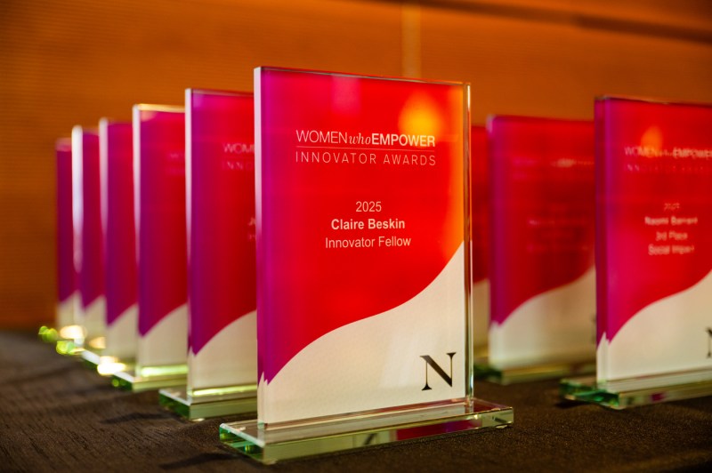Rectangular glass red-and-white awards for the 2025 Innovator Awardees stand in rows on a table.