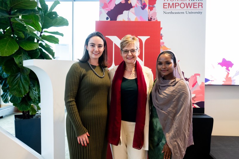 Three women pose for a photo in front of the branded summit decorations.