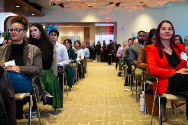 A wide shot of the ballroom shows rows of women seated on both sides of the central aisle.