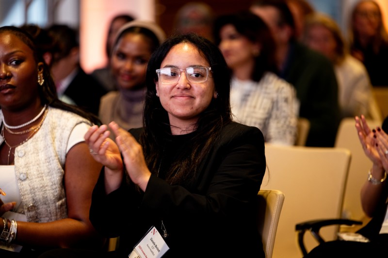 A woman seated in the audience smiles and applauds during the event. 