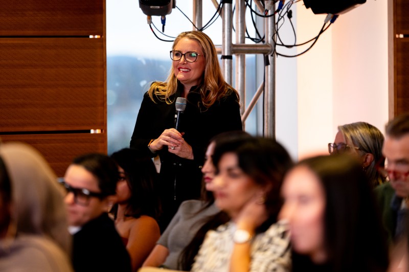 A woman stands in the audience with a microphone asking a question.