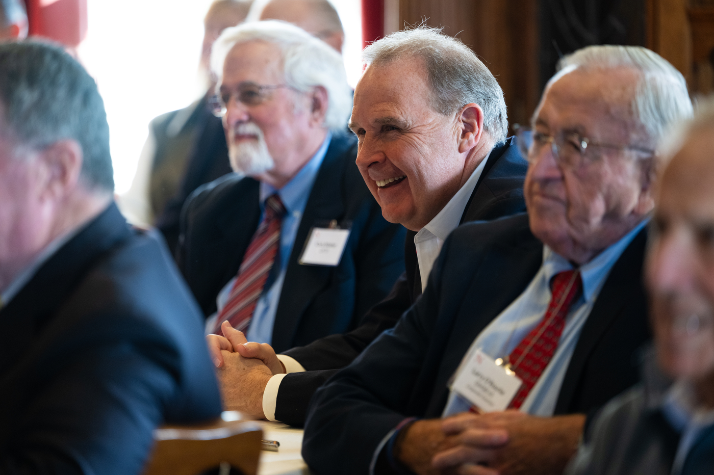 A group of older attendees sit in rows during an event; several smile and look toward the front of the room.