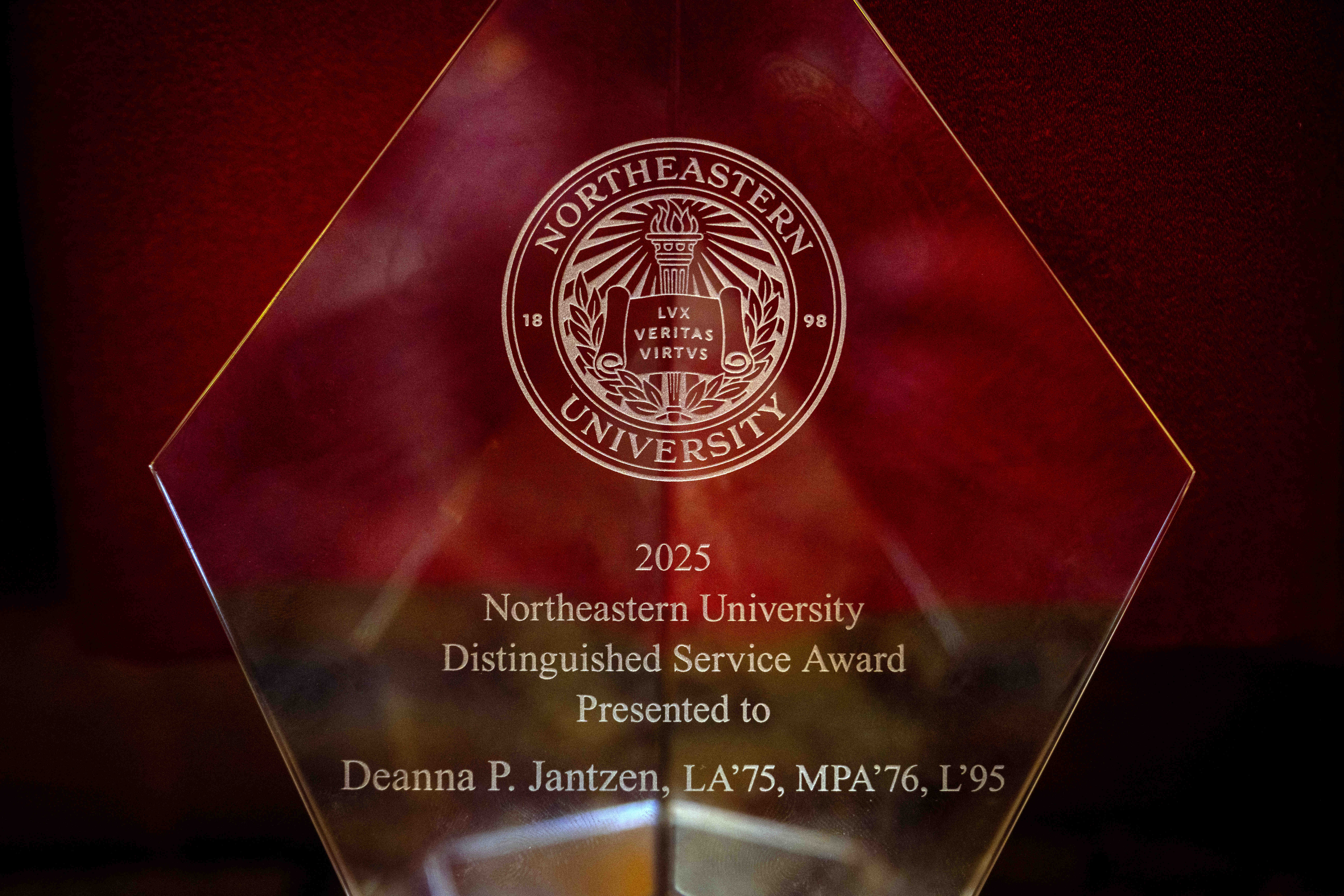 A close-up of a glass award engraved with a Northeastern University seal, displayed against a red background.