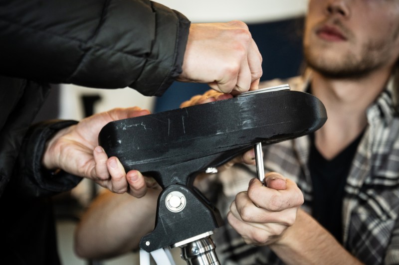 Close-up of hands adjusting or repairing a rowing oar handle, with the grip and blade connection visible.