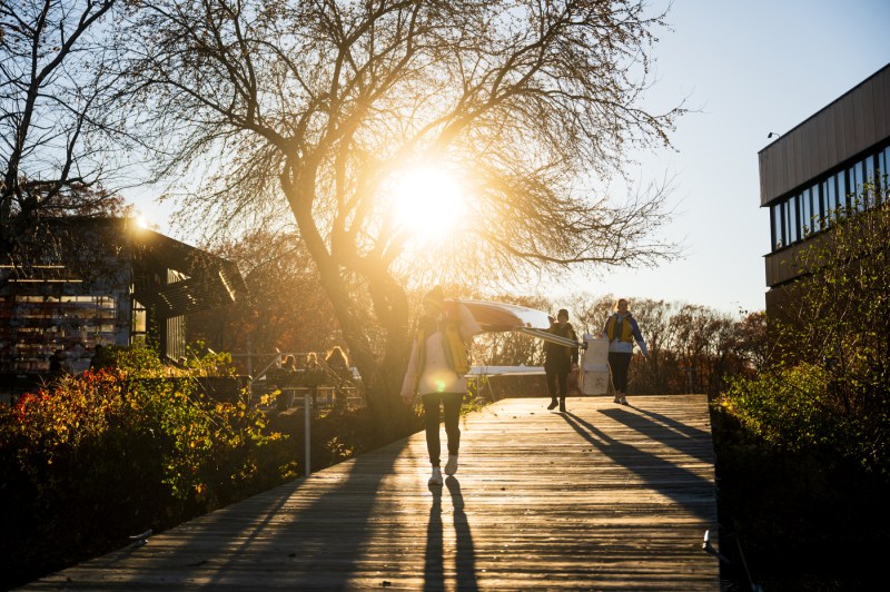 Members of CRI rowing carry a double skull down to the Charles River on a wooden bridge.