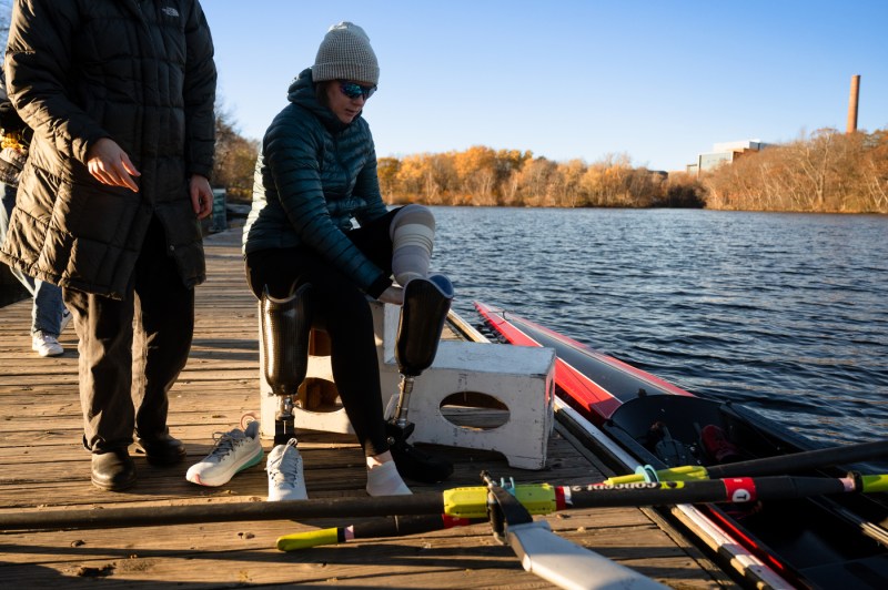 Megan Hopkins, a para-athlete, sits to put on the prosthetic foot and ankle designed specifically for rowing by Northeastern bioengineering undergraduate students, before testing it on the Charles River on Tuesday, Nov. 18, 2025.