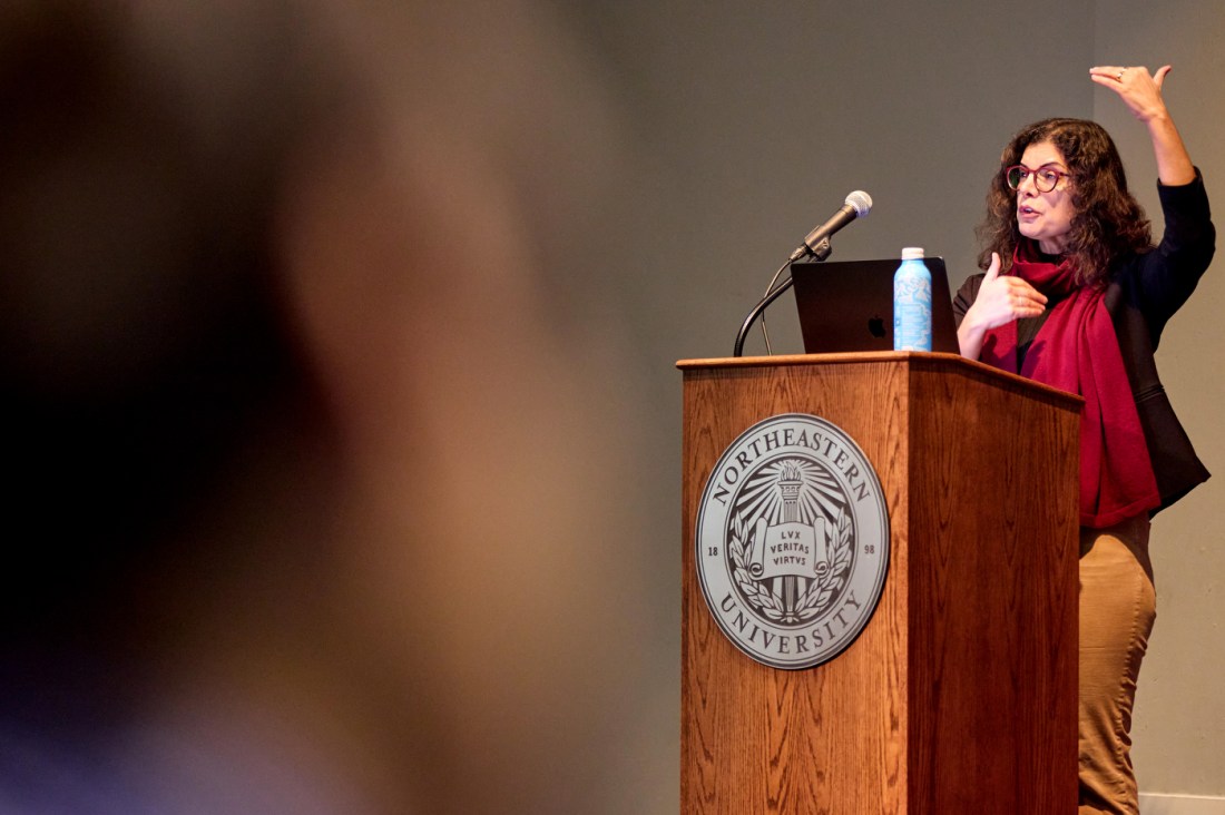Tina Eliassi-Rad speaking at a podium with the Northeastern seal on it.