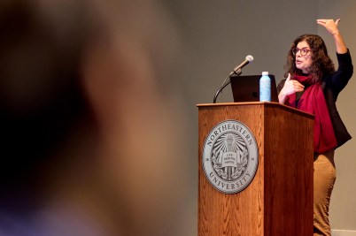Tina Eliassi-Rad speaking at a podium with the Northeastern seal on it.
