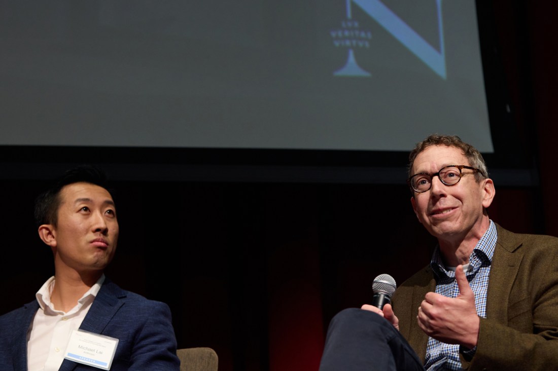Three panelists sit onstage, smiling and speaking into microphones during a Northeastern University event.