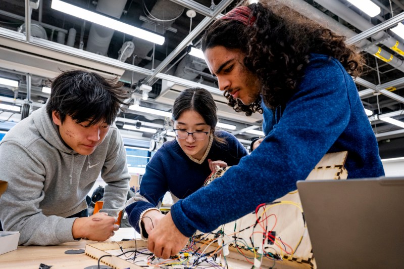 Three students do electrical work at a workbench in the Makerspace.