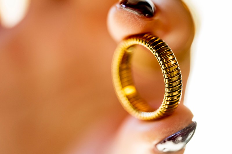 Two fingers with dark nail polish hold a gold-toned ring.