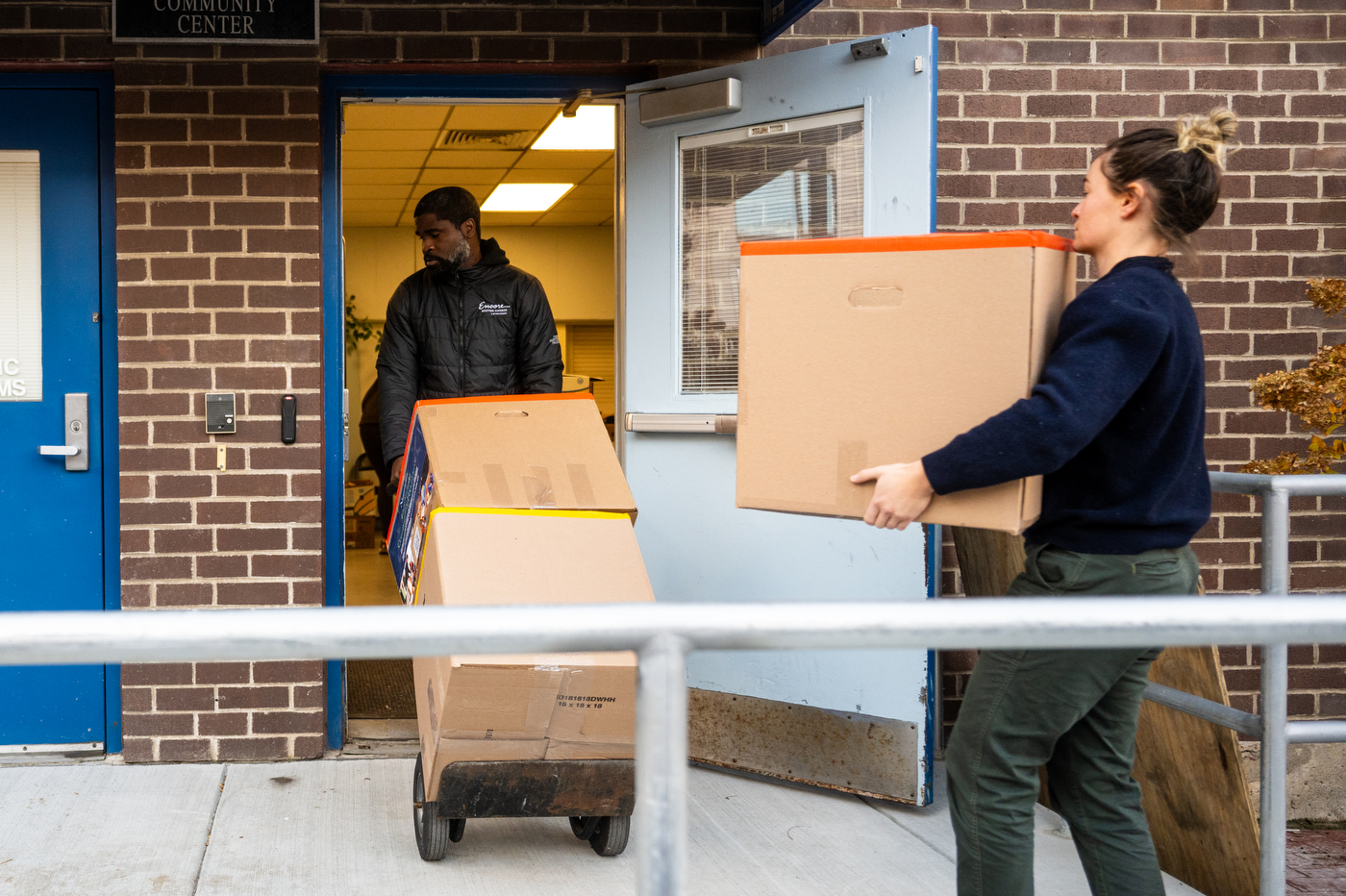 A person carries a cardboard box while another person rolls cardboard boxes.