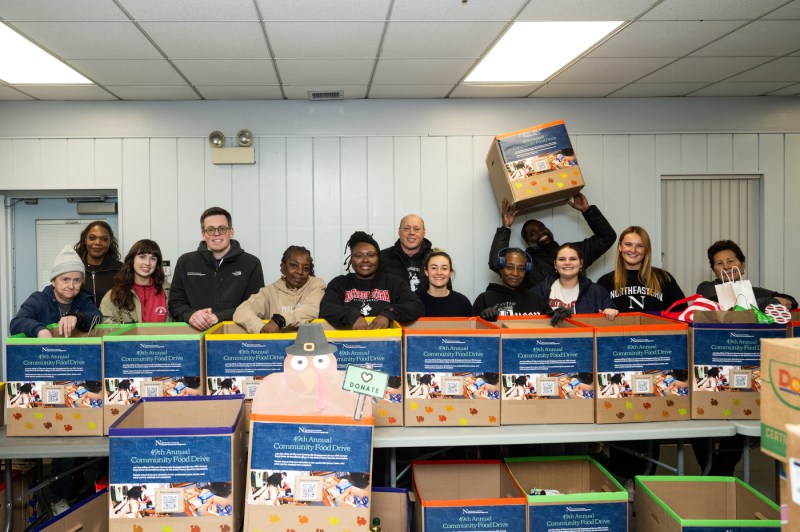 A team of people pose for a photo with cardboard boxes for a food drive.