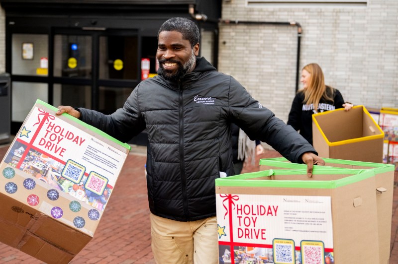A person carries two cardboard boxes for a food drive outside.