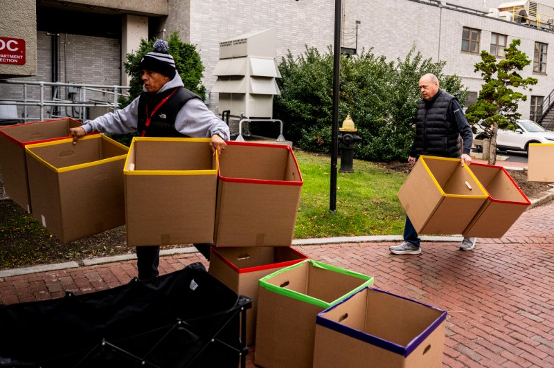 Two people dressed in winter clothing carry several cardboard boxes for a food drive.