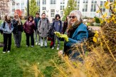 A group of Northeastern students stand outside in the grass on campus while listening to a woman speak.