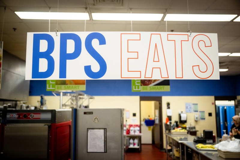 A large wall sign reading 'BPS EATS' with 'BPS' in solid blue letters and 'EATS' in outlined letters, mounted above what appears to be a cafeteria serving area with fluorescent lighting.