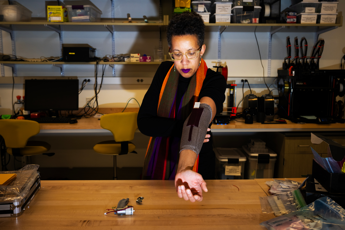 Kris Dorsey stands in a lab wearing an adaptive splint on one arm that she is holding outstretched in front of her. 
