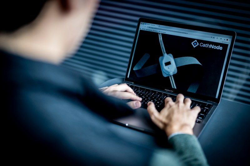 A student works on a laptop. The laptop screen shows the text "CathNode" and a model.