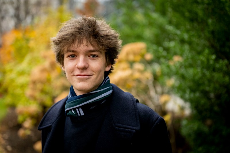 A person wearing a winter jacket and scarf poses for a photo outside.