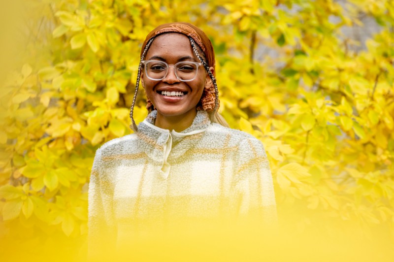 A person poses for a photo outside near bright yellow foliage.