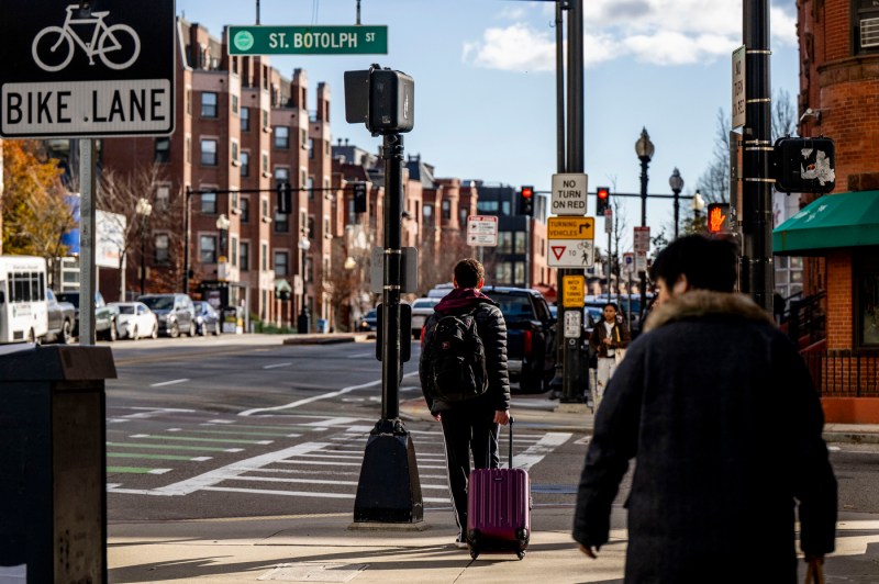 A student wheels a suitcase down the sidewalk.