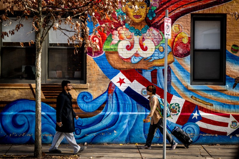 A student wheels a suitcase down the sidewalk. Another person walks toward that student.