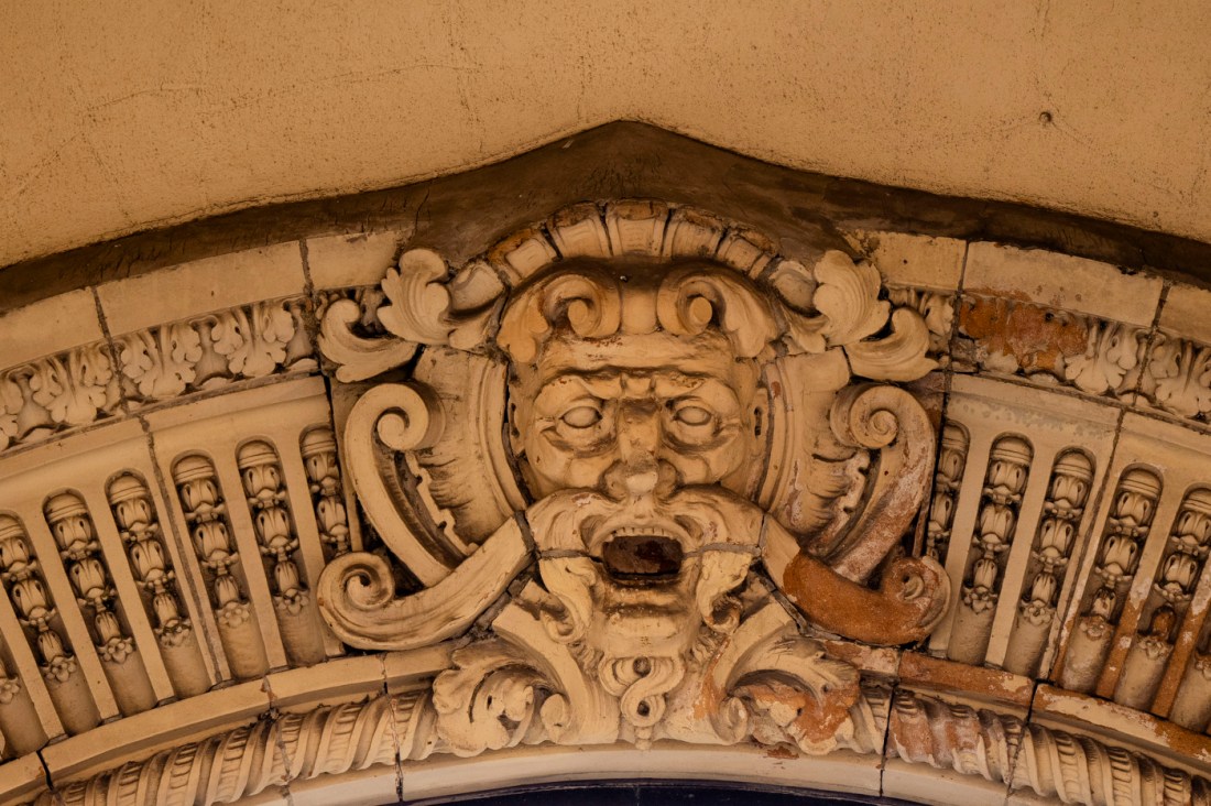 A terra cotta sculptural detail of a stylized face within the ornamental arch of Matthews Arena.