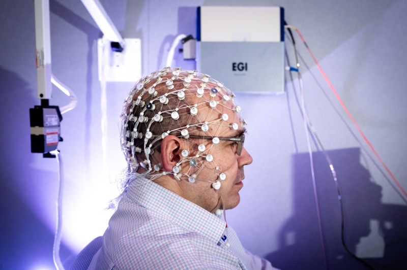 A professor wears an electrode cap on his head in a lab.