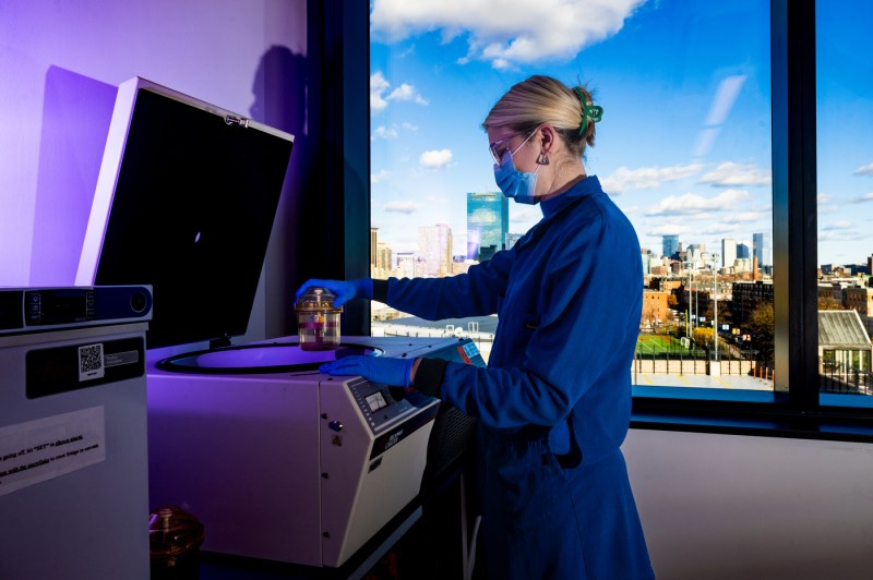 A person wearing blue gloves, a lab coat and a mask holds blood samples. 