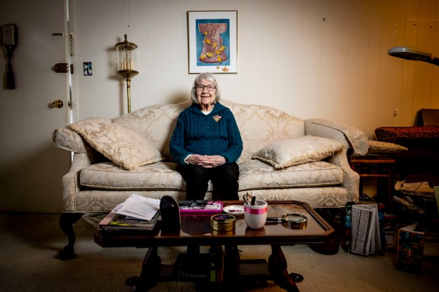 Ruth Gove, a 100 year-old woman, sitting on her sofa and smiling.