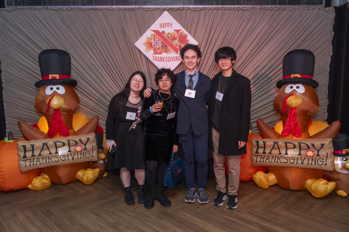 Four people pose with 'Happy thanksgiving' banners and inflatable turkeys