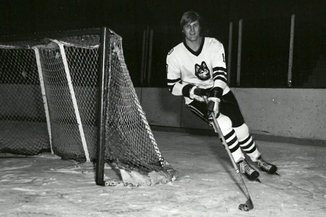 A black and white photo of David Sherlock on the ice, skating around the goal